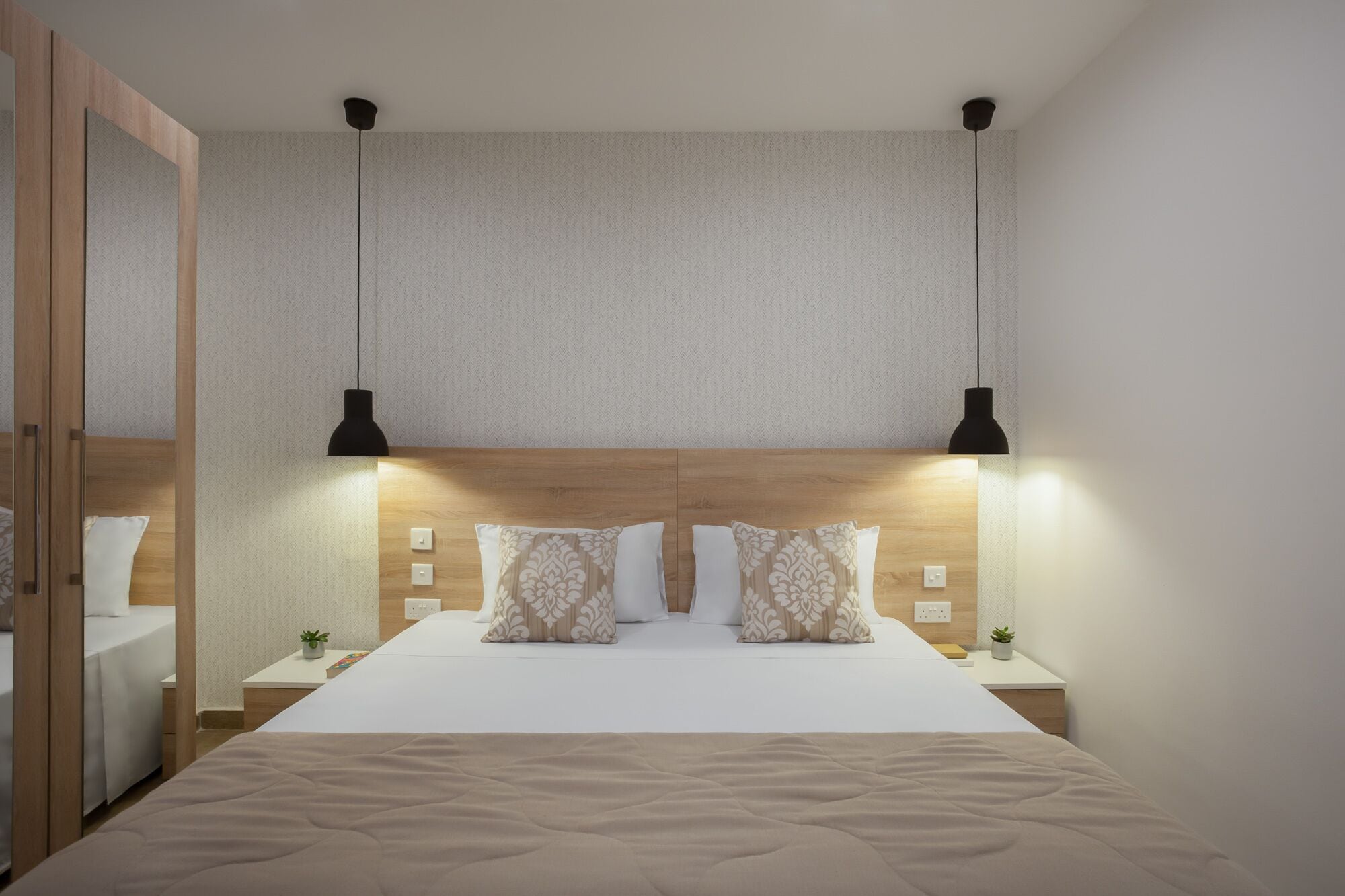 Une chambre à coucher bien aménagée, avec un grand lit, deux tables de chevet, une tête de lit en bois et deux lampes suspendues.
