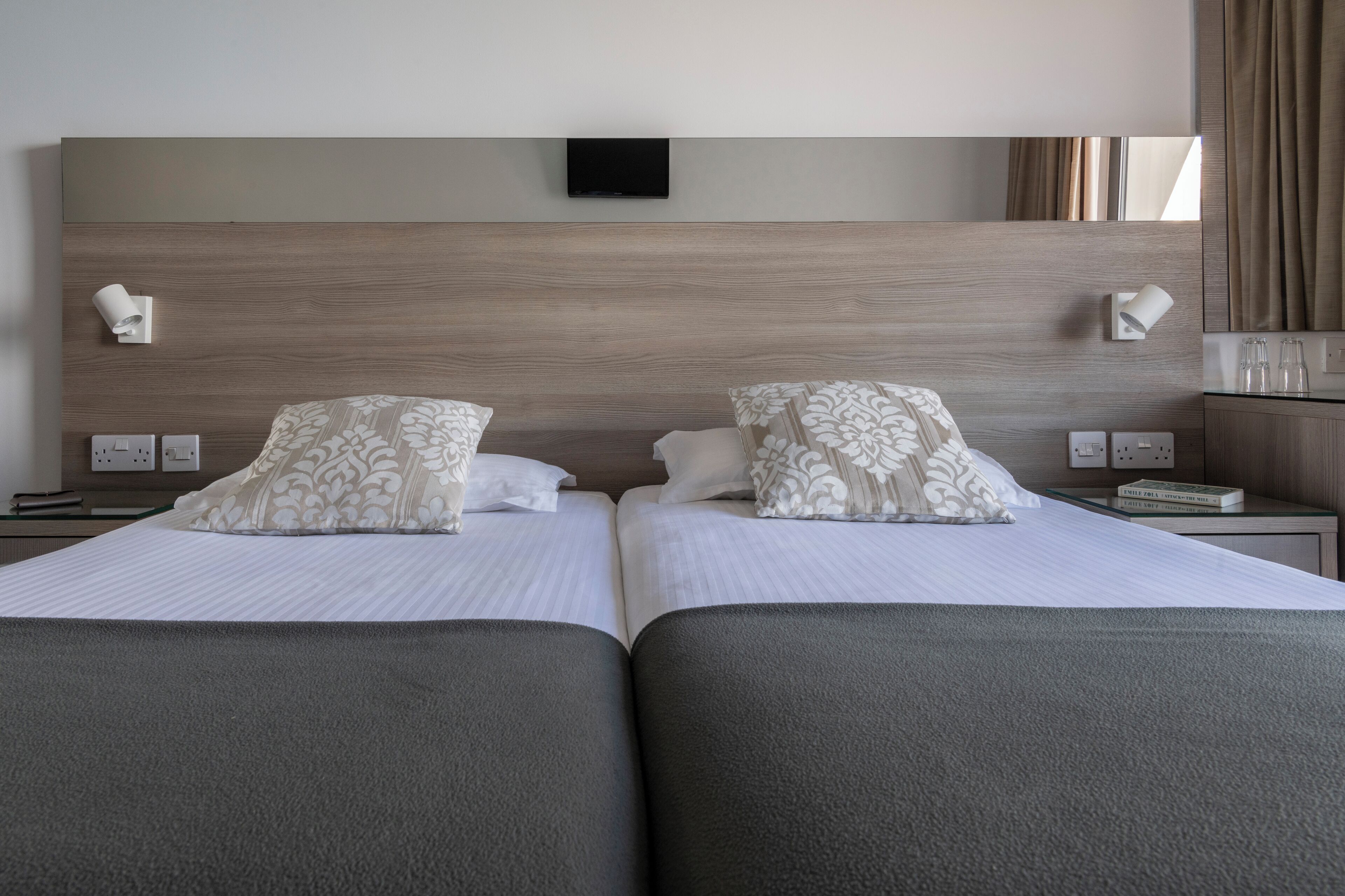 Une chambre d’hôtel avec deux lits, un téléviseur à écran plat fixé au-dessus de la tête de lit, des lampes de chevet et un miroir.