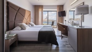 Habitación de hotel con dos camas, un escritorio, televisión y vista a la ciudad.