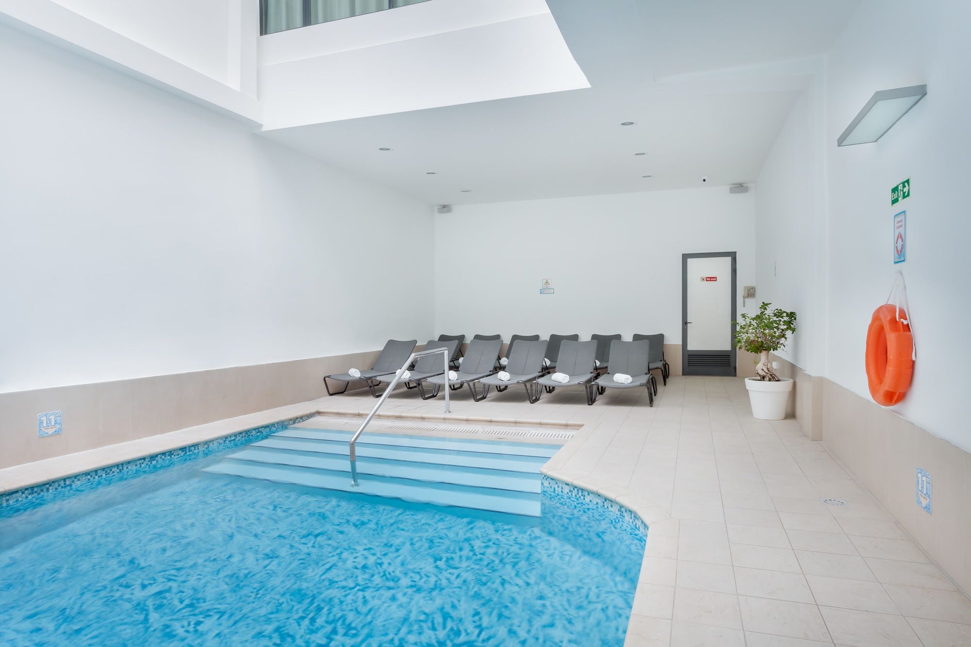 A pool area with lounge chairs and a door leading to an exit.