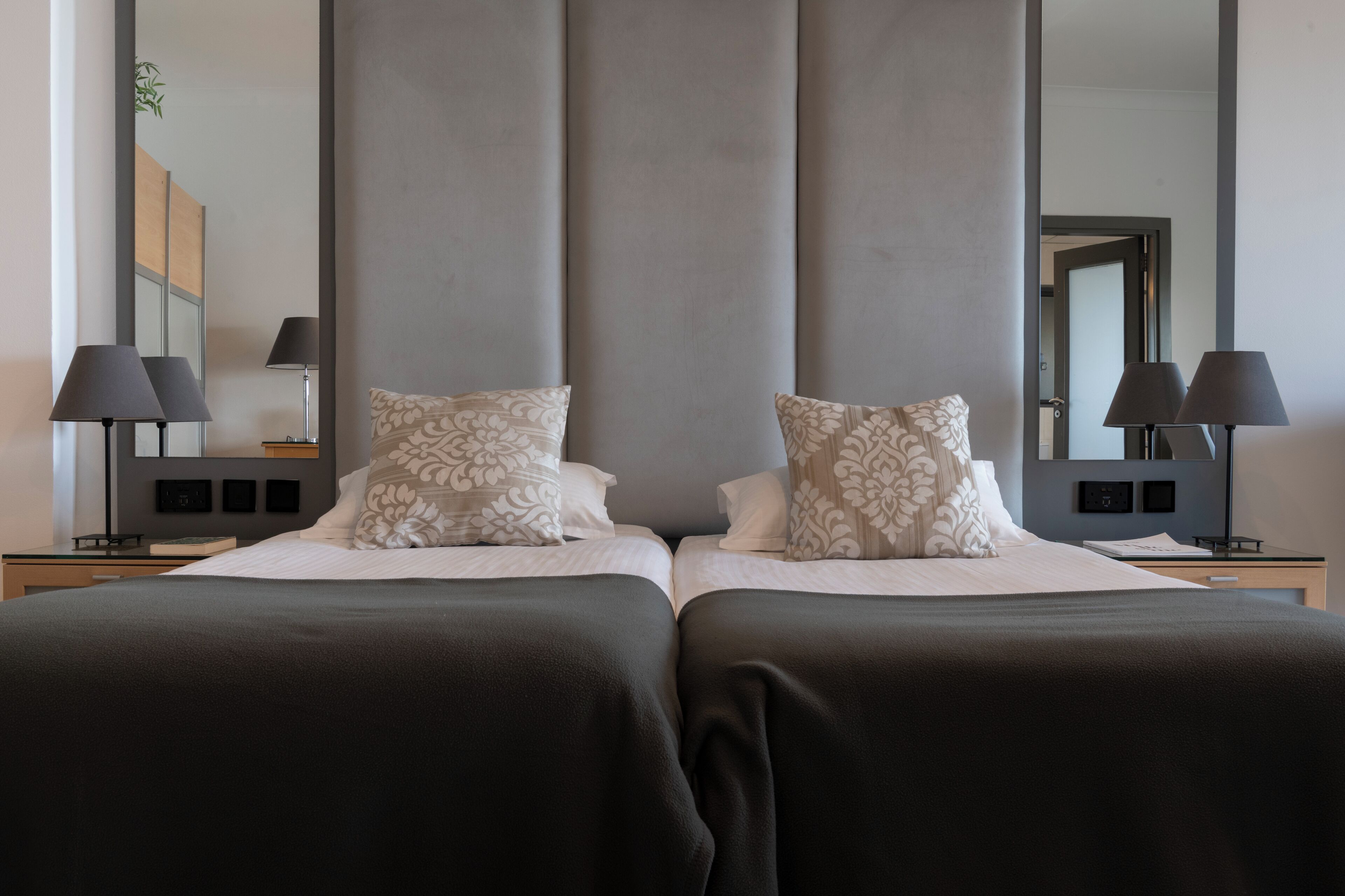 A double bed with a dark bedspread and patterned pillows, flanked by nightstands with lamps.