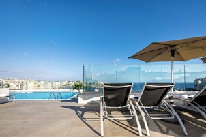 A rooftop terrace with a pool, two lounge chairs, and an umbrella.