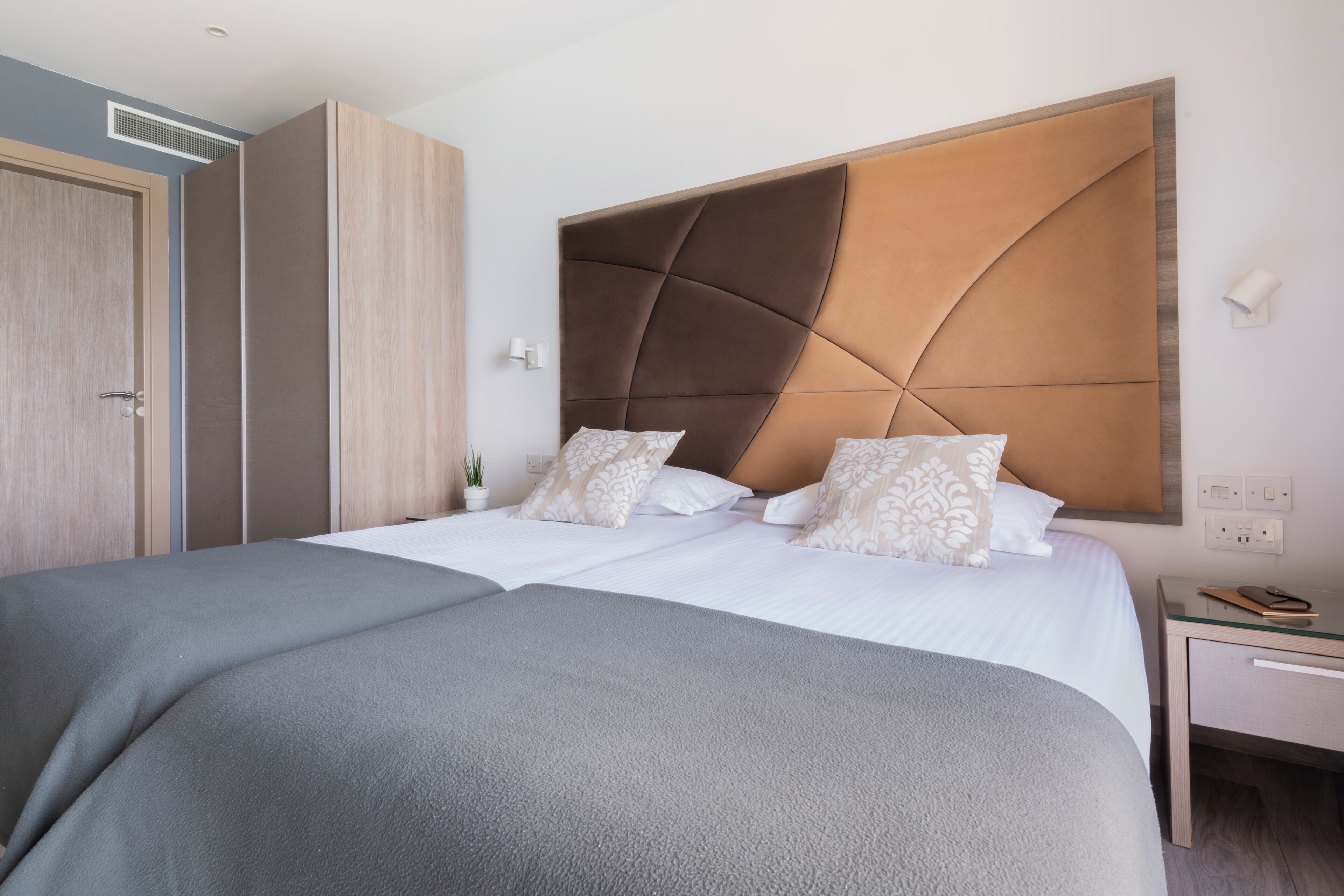 Una cama doble con cabecera moderna, una mesita de noche con lámpara y un armario.