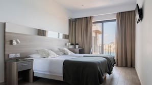Habitación de hotel moderna con una cama grande, mesitas de noche, un escritorio pequeño, una planta en maceta y vistas de la ciudad a través de amplias ventanas.