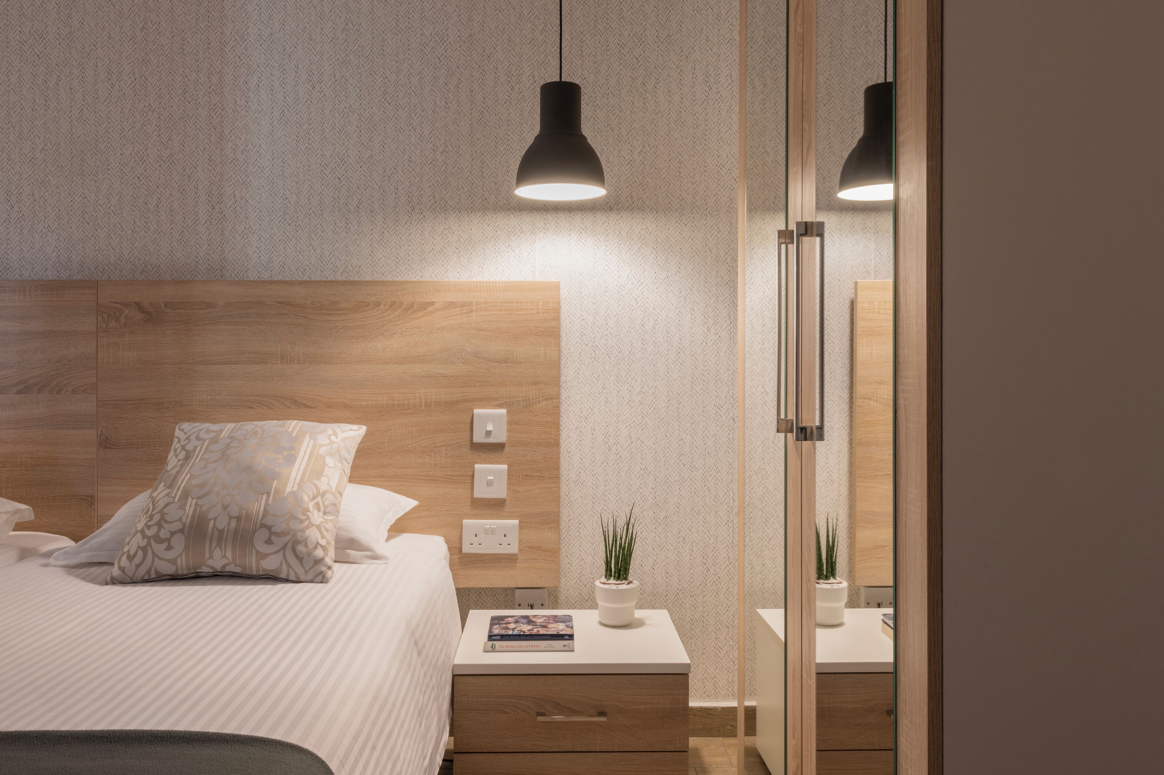 Ein modernes Schlafzimmer mit einem hölzernen Kopfteil, einem Nachttisch mit Pflanze und einer Nachttischlampe.