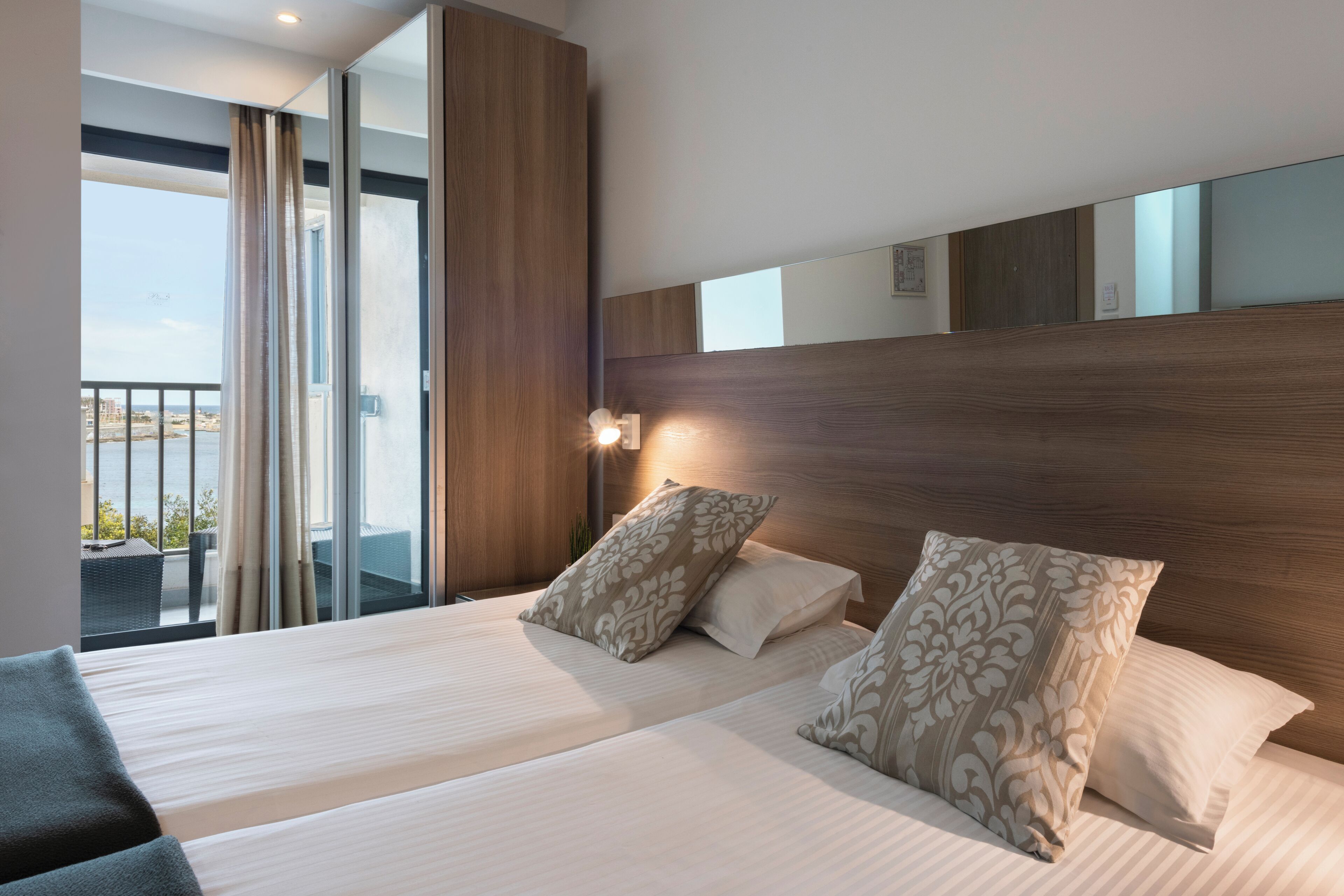 A hotel room with two beds, a wooden headboard, a large window with a view, and a balcony.