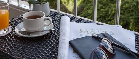 A table with a cup of tea, a glass of orange juice, a book, a pair of sunglasses, and a small potted plant.