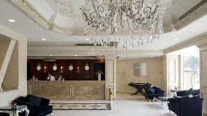 A hotel lobby with a grand chandelier, a reception desk, and seating areas.