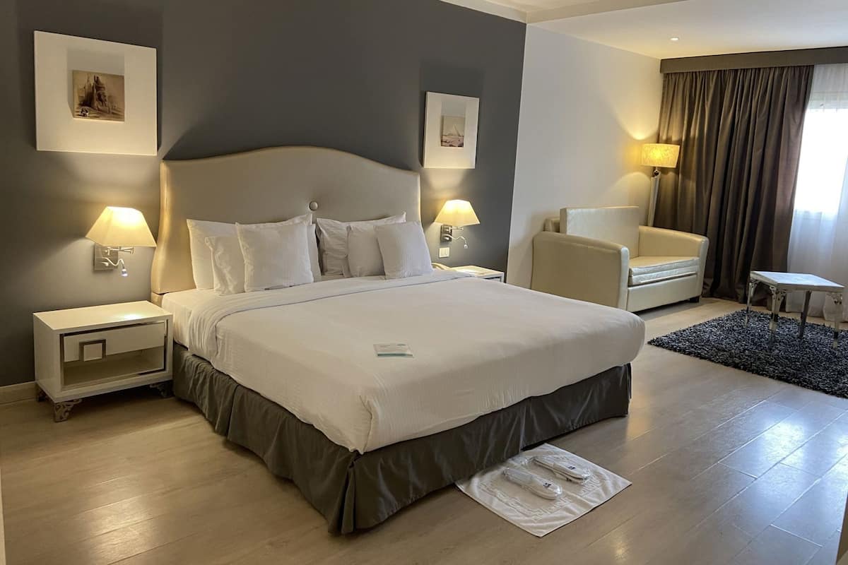 A hotel room with a large bed, two bedside tables with lamps, a chair, a small table, and a rug.