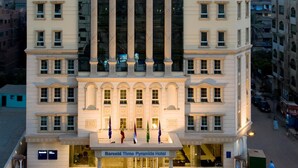 A tall, multi-story hotel with a classical facade, large windows, and a prominent entrance with flags.