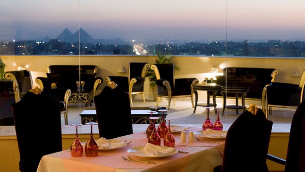 A dining area with tables set for two, chairs, and a view of a cityscape with mountains in the background.