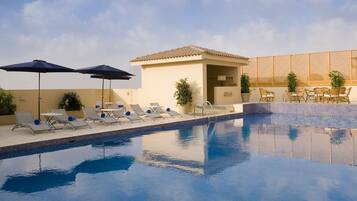 Una piscina al aire libre, sombrillas, sillones reclinables de piscina