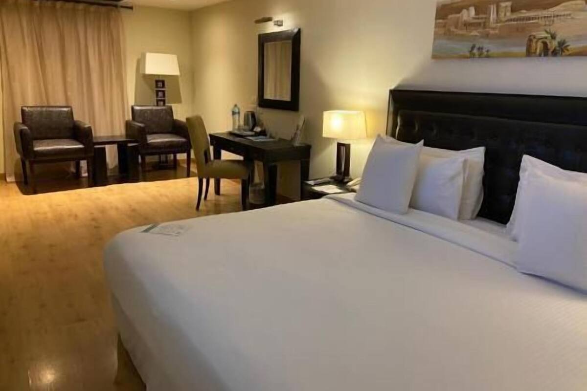 A hotel room with a bed, a desk, a chair, a lamp, and a painting on the wall.