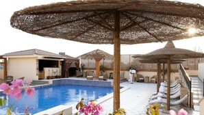 A pool area with lounge chairs, a covered seating area, and a building with a sign.