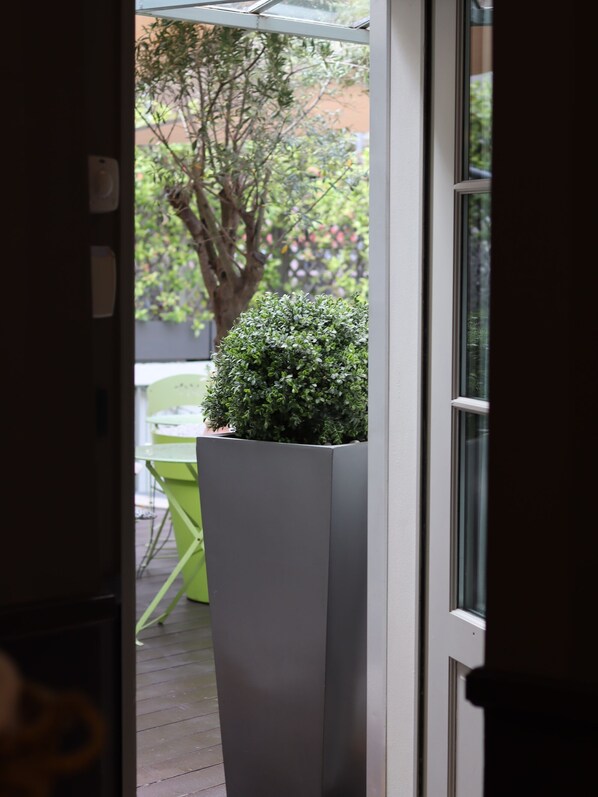 Une vue à travers une porte donnant sur un patio, où l’on aperçoit une chaise verte et un pot de fleurs.