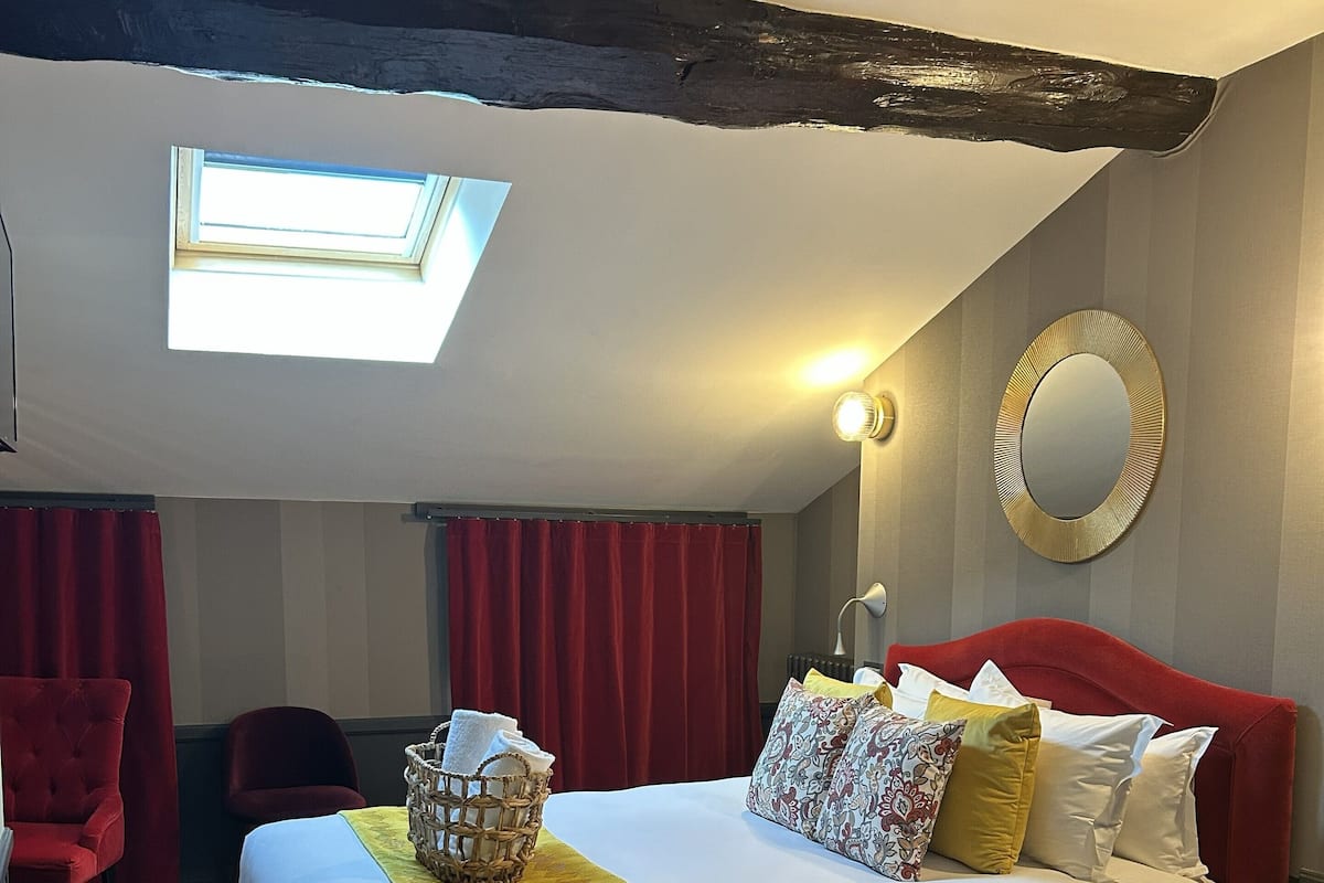 Una camera d'albergo con un letto grande, una poltrona rossa, un tavolino, una lampada e uno specchio a parete.