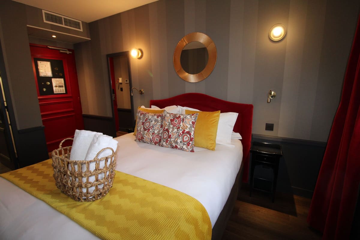 Una camera d'albergo con un letto grande, una testata rossa, uno specchio rotondo appeso al muro e un comodino.