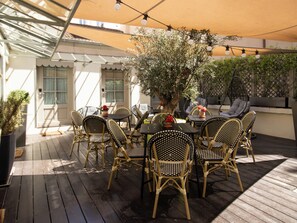 Una terrazza esterna con mobili in vimini, un tavolo al centro e un albero in vaso.