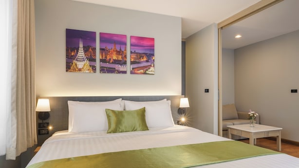 A hotel room with a large bed, two wall-mounted lamps, a nightstand, a small table with a vase, and two framed pictures of a temple. - iCheck inn Residence soi 2 (Bangkok)