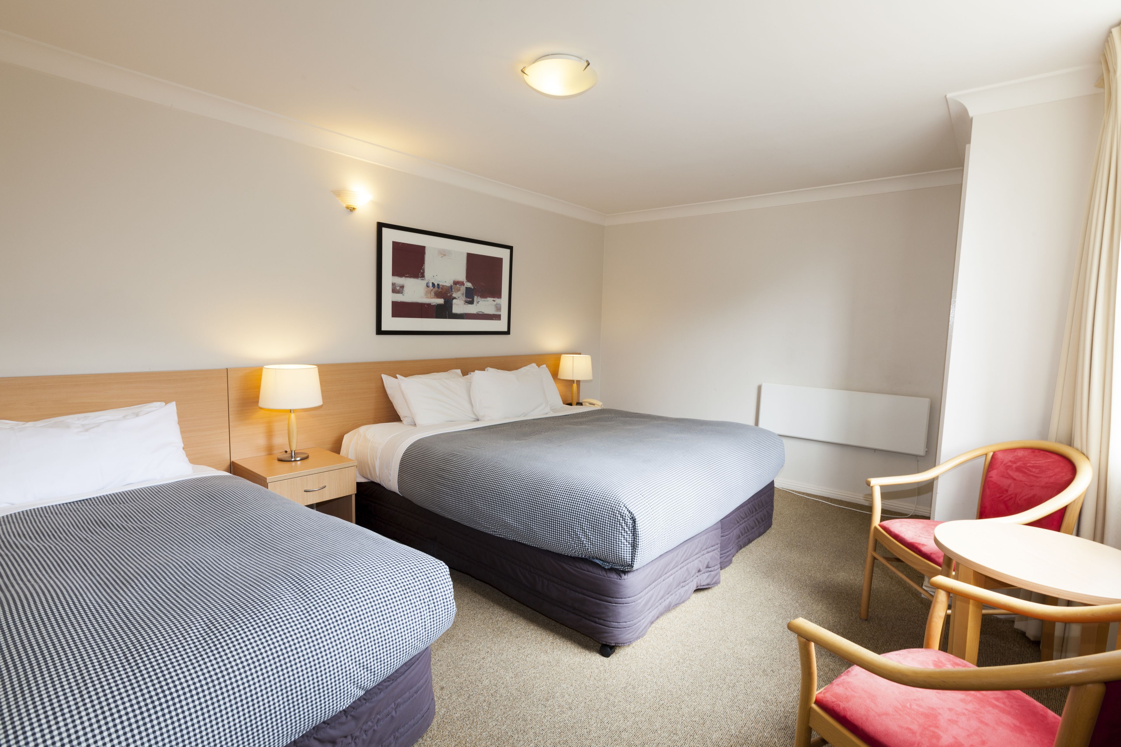 Ein Hotelzimmer mit zwei Betten, einem Schreibtisch, einem Sessel und einem Bild an der Wand.