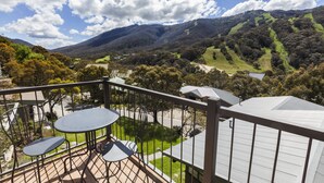 A balcony with a table and chairs, overlooking a valley with hills and trees. - The Denman Hotel (Thredbo)
