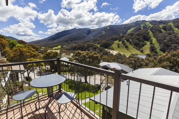 A balcony with a table and chairs, overlooking a valley with hills and trees. - The Denman Hotel (Thredbo)