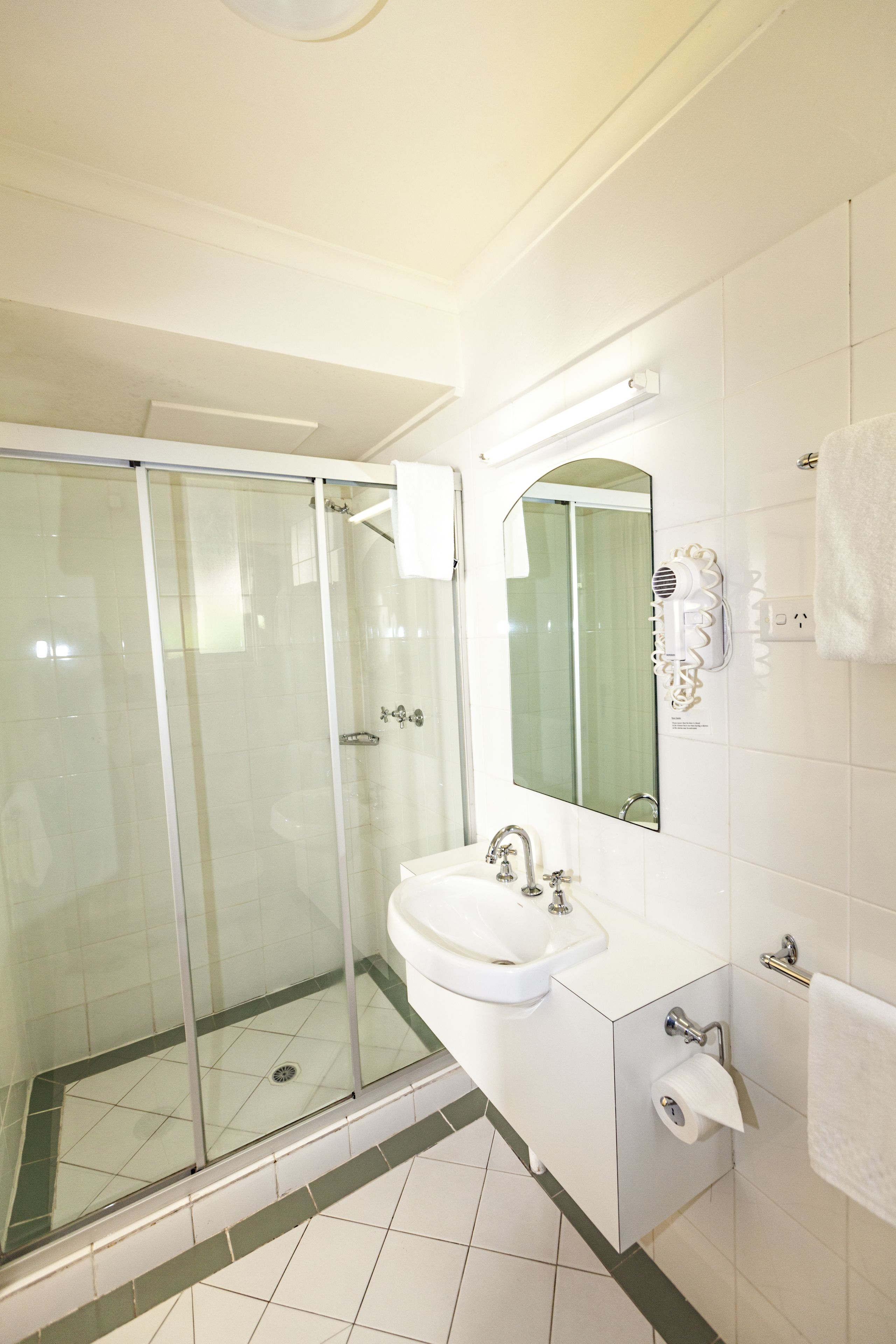 Ein Badezimmer mit Duschkabine, Waschbecken, Spiegel und Handtuchhalter.