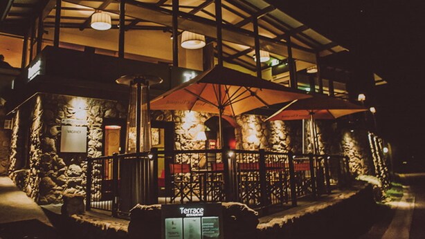 A terrace restaurant with stone walls, outdoor seating, and umbrellas. - The Denman Hotel (Thredbo)