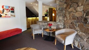 A modern interior with a stone accent wall, a red bench, and two armchairs around a small wooden table with a vase of red flowers. - The Denman Hotel (Thredbo)