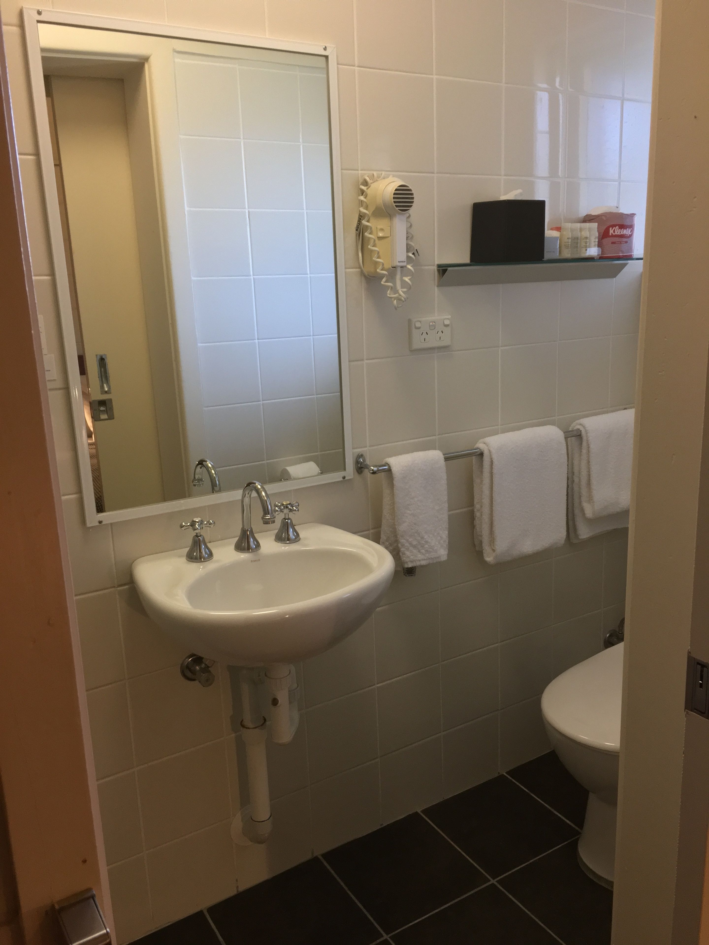 Ein Badezimmer mit einem weißen Waschbecken, einem Spiegel, einem Haartrockner und einer Toilette.