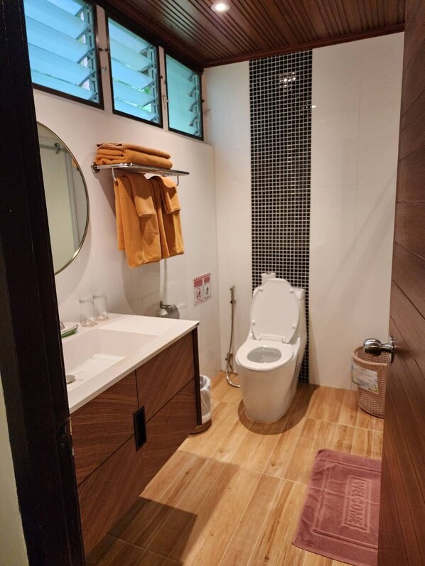 Un baño pequeño con tocador de madera, inodoro y una ventana discreta.
