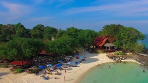 An aerial view of a beach with a restaurant and umbrellas, surrounded by lush greenery and a clear view of the sea. - Phi Phi Natural Resort (Ko Phi Phi)