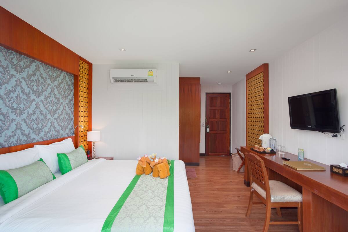 A hotel room with a large bed, a desk, a television, and an air conditioning unit.