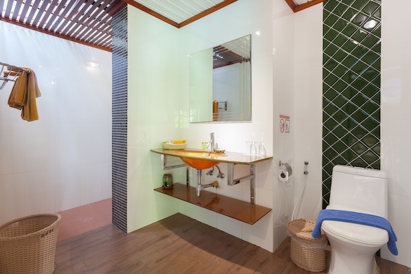 A bathroom with a wooden vanity, a glass sink, a mirror, a toilet, and a shower area.