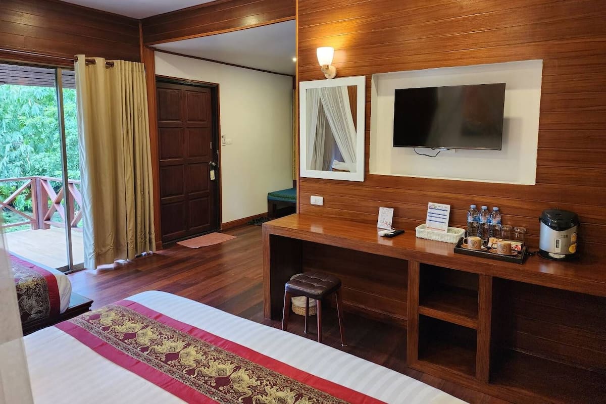 A hotel room with a bed, a desk with a flat-screen TV, a coffee maker, and a small table with a basket.