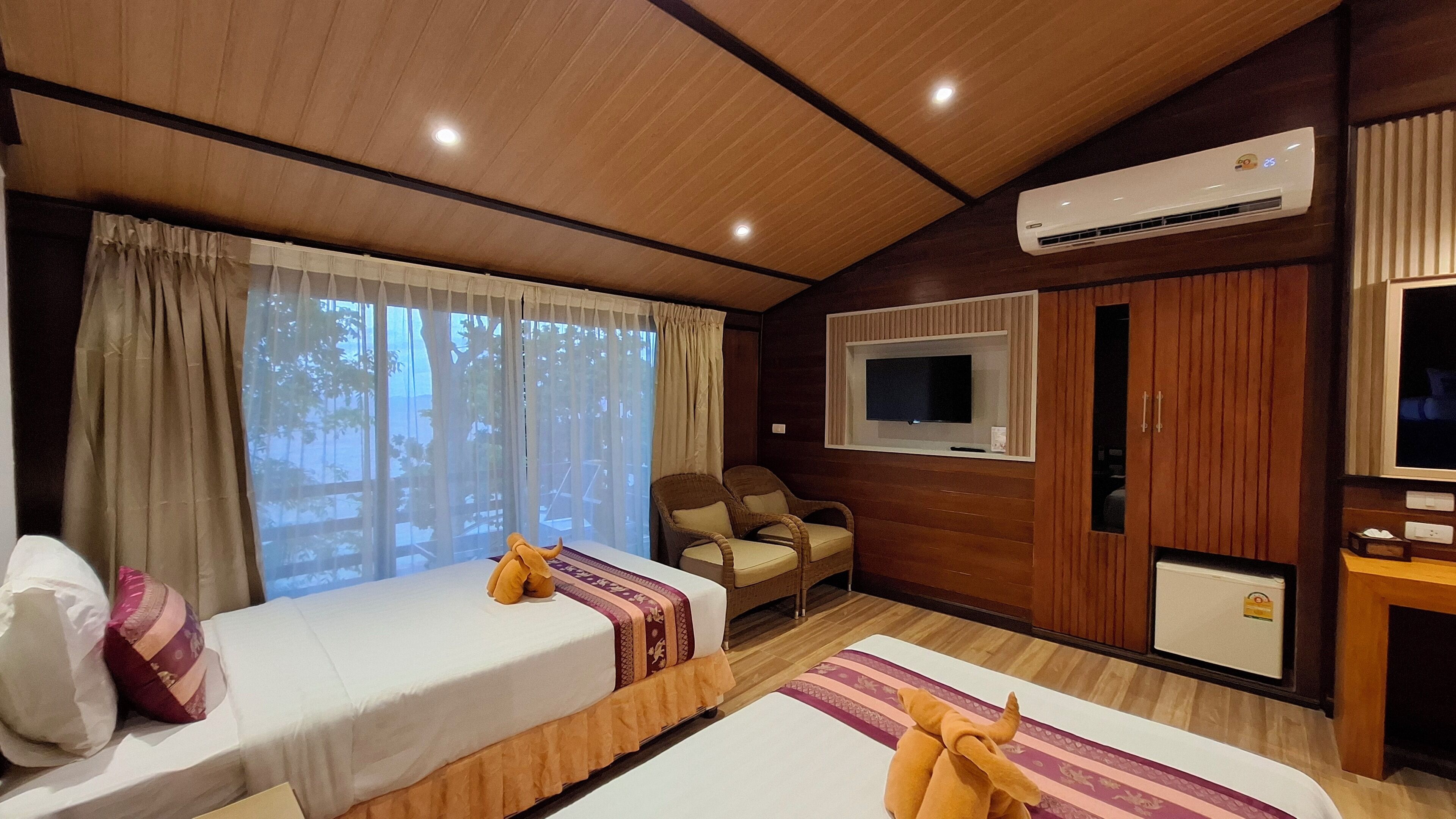 A hotel room with two beds, a TV, a wardrobe, and an air conditioning unit.