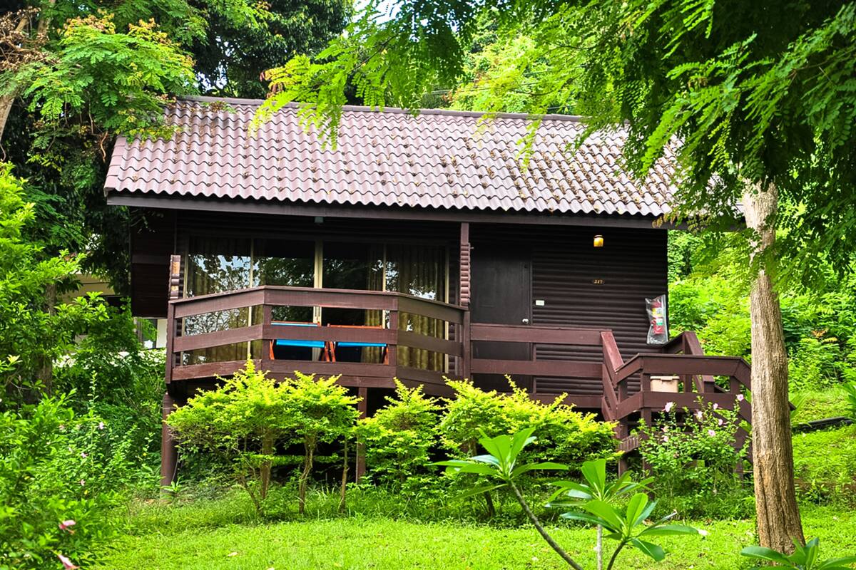 A wooden house with a tiled roof, surrounded by lush greenery.