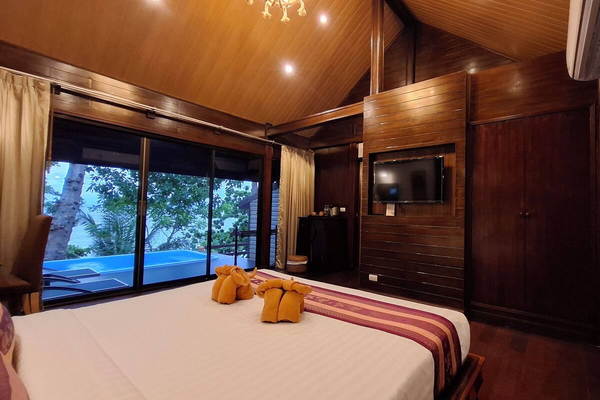 A spacious bedroom with a large bed, a television mounted on the wall, and a view of the outdoors through large sliding doors.