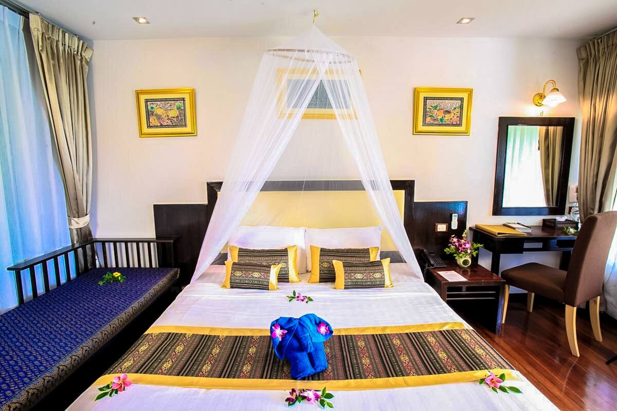 A hotel room with a large bed, a desk, a chair, a computer, and a window with curtains.