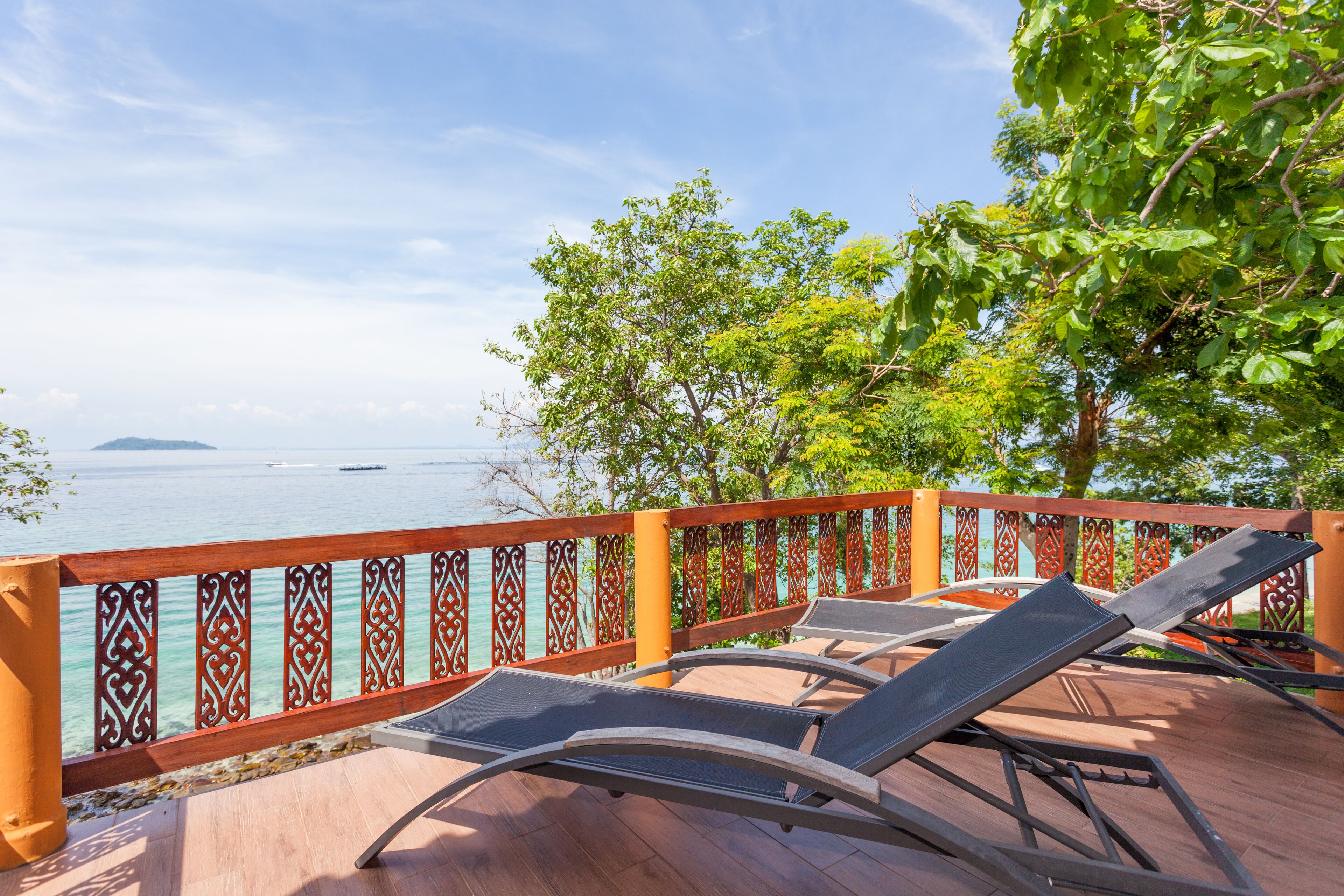 Terraza con sillones de descanso con vista a un cuerpo de agua, barandilla decorativa y exuberante vegetación.