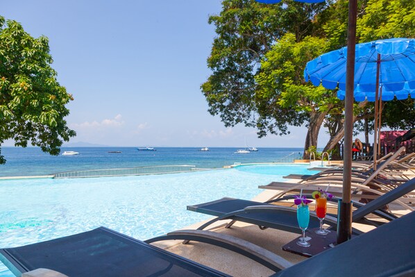 Un área junto a la piscina con sillones de descanso, una piscina y vistas al mar.