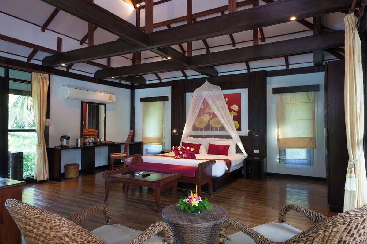 A spacious room with a large bed, a sitting area with wicker furniture, and a kitchenette.