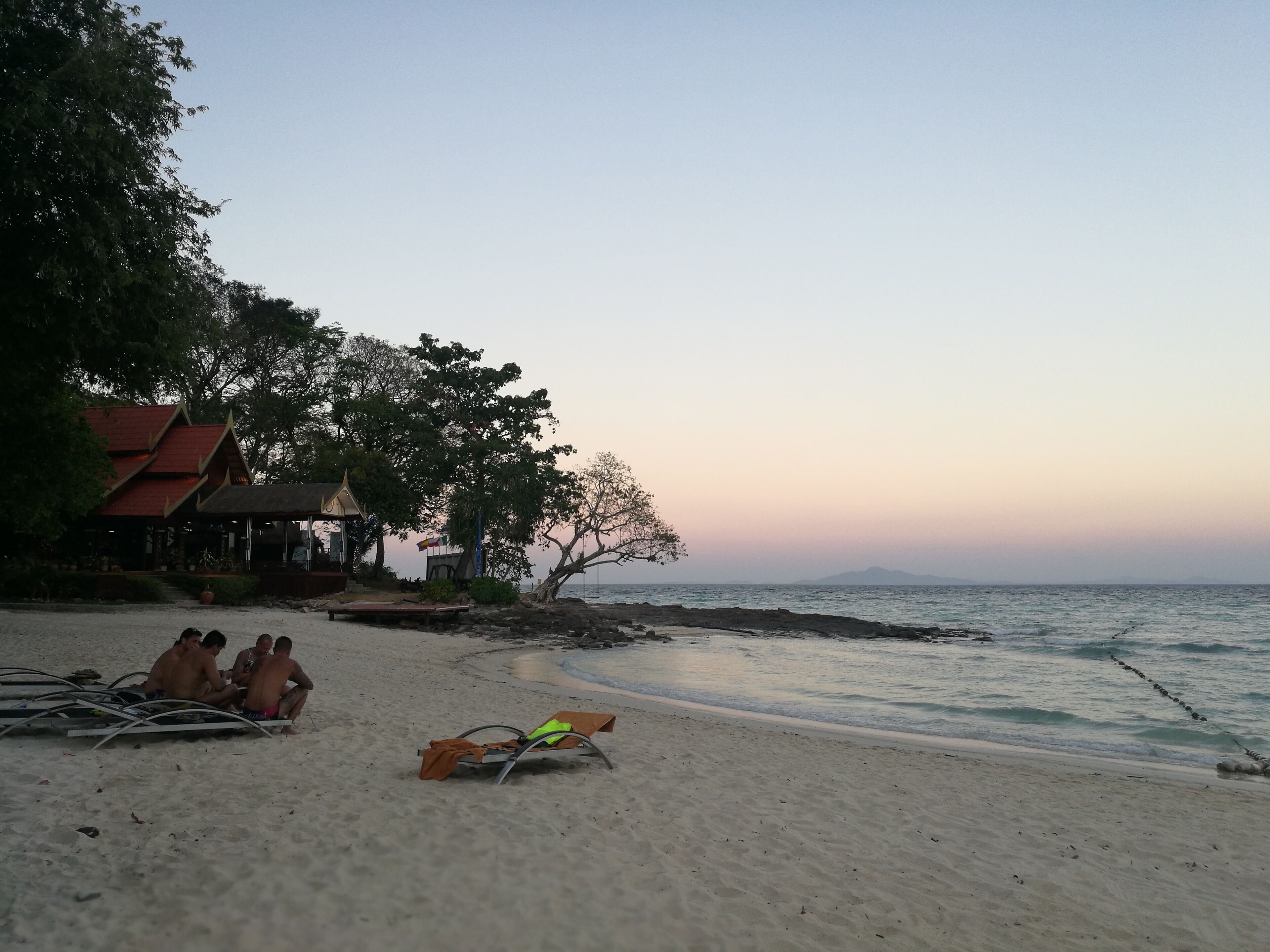 A beach with a traditional building and a tree.