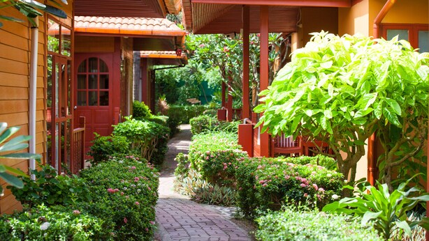 A pathway flanked by lush greenery and traditional wooden buildings with red roofs and doors. - P. P. Erawan Palms Resort (Ko Phi Phi)