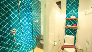 A bathroom with a glass-enclosed shower, a toilet, and a shelf with toiletries.
