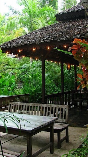 An outdoor seating area with a thatched roof, surrounded by lush greenery. - Fern Resort (Mae Hong Son)