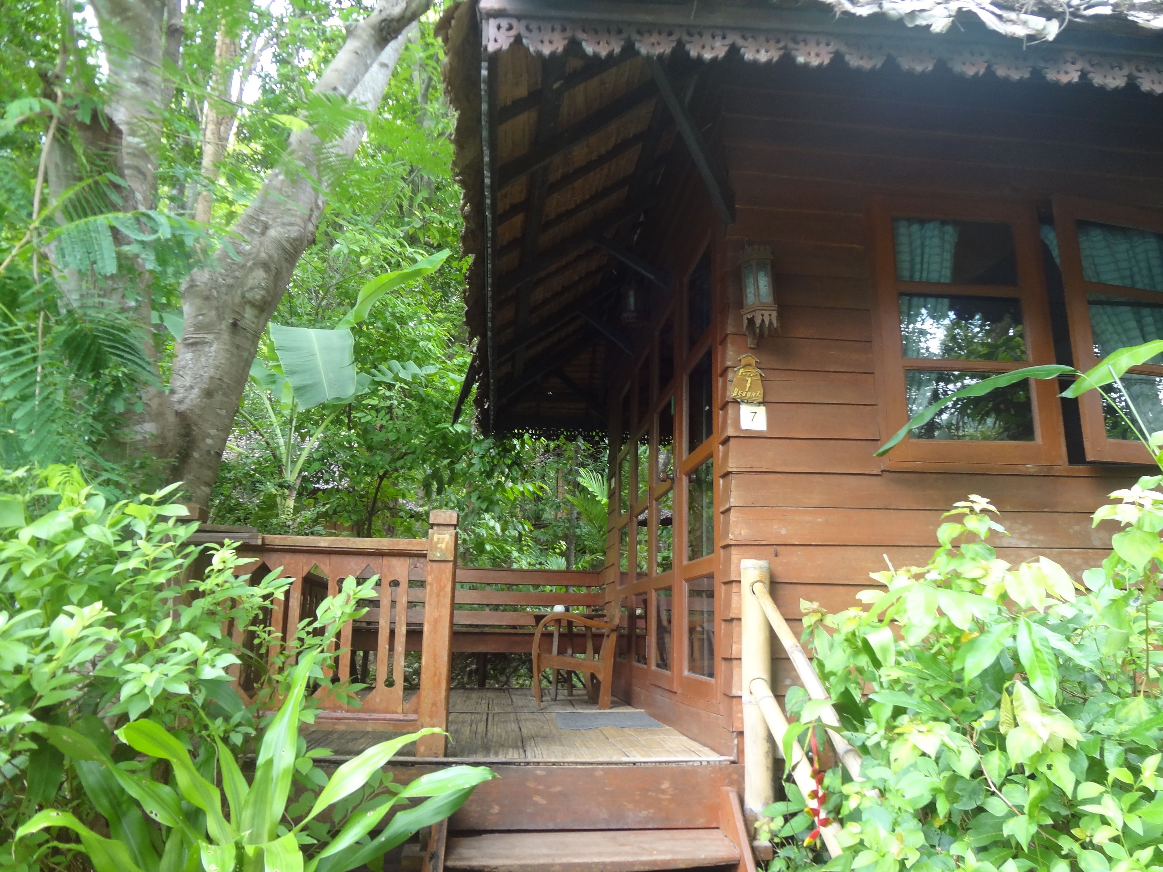 A wooden building with a porch, surrounded by lush greenery.
