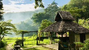 A rustic wooden structure with a thatched roof, surrounded by lush greenery and a clear sky. - Fern Resort (Mae Hong Son)