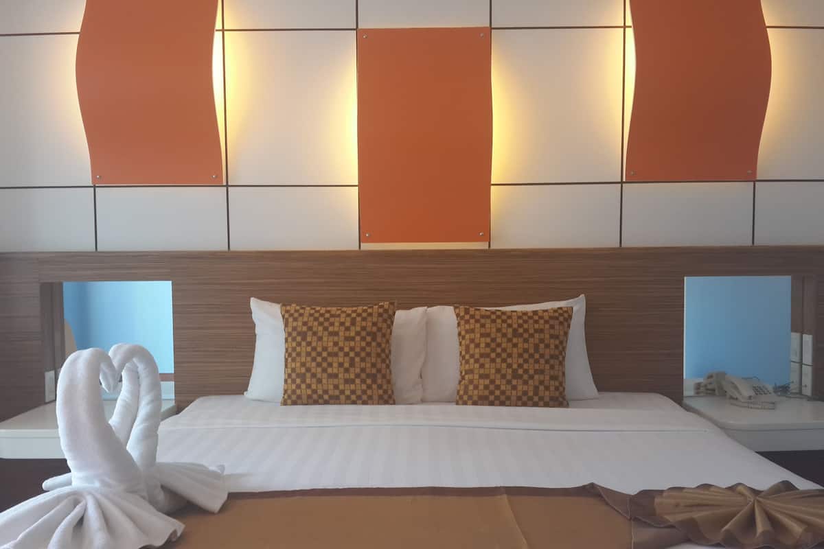 A hotel room with a large bed, two pillows, a bedside table with a phone, and a wall with illuminated panels.