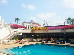 A pool area with lounge chairs and a staircase leading to a building with a dome and flowers. - Caesar Palace Hotel (Pattaya)